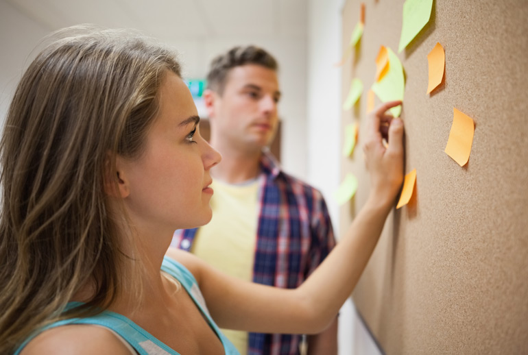 A product owner shows a stakeholder how a Scrum project will work via post-its on a board.