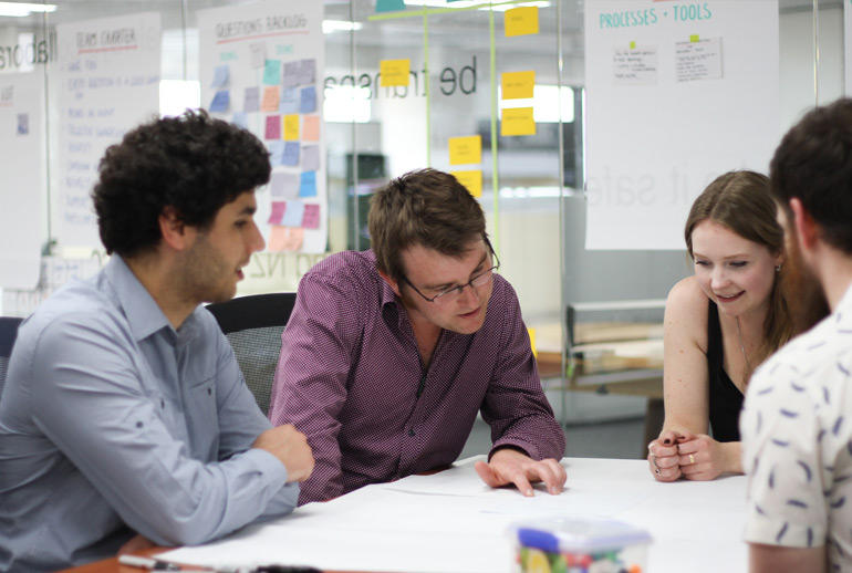 A product discovery team discuss their Elevator Pitch round a table. 