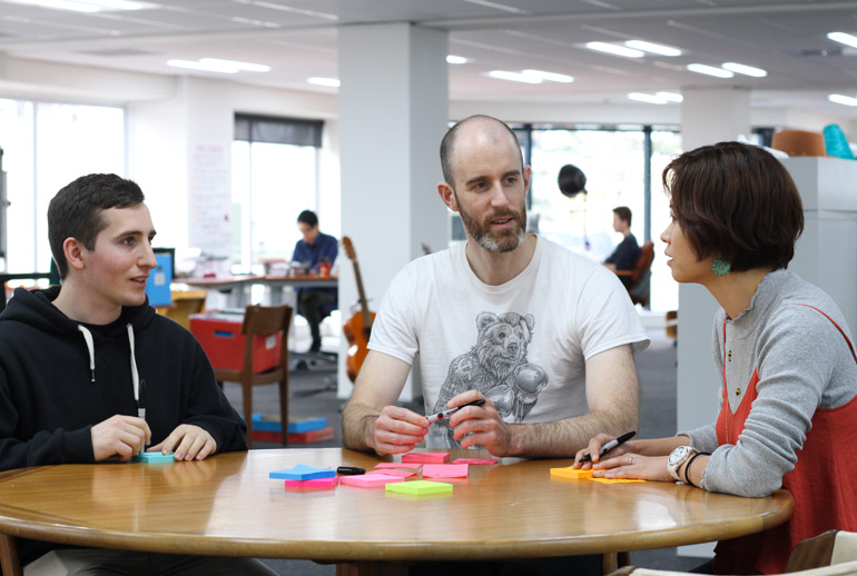 A team discuss user story tasks with post-its at a table. Conversation is one of the key features of user stories in Scrum. 