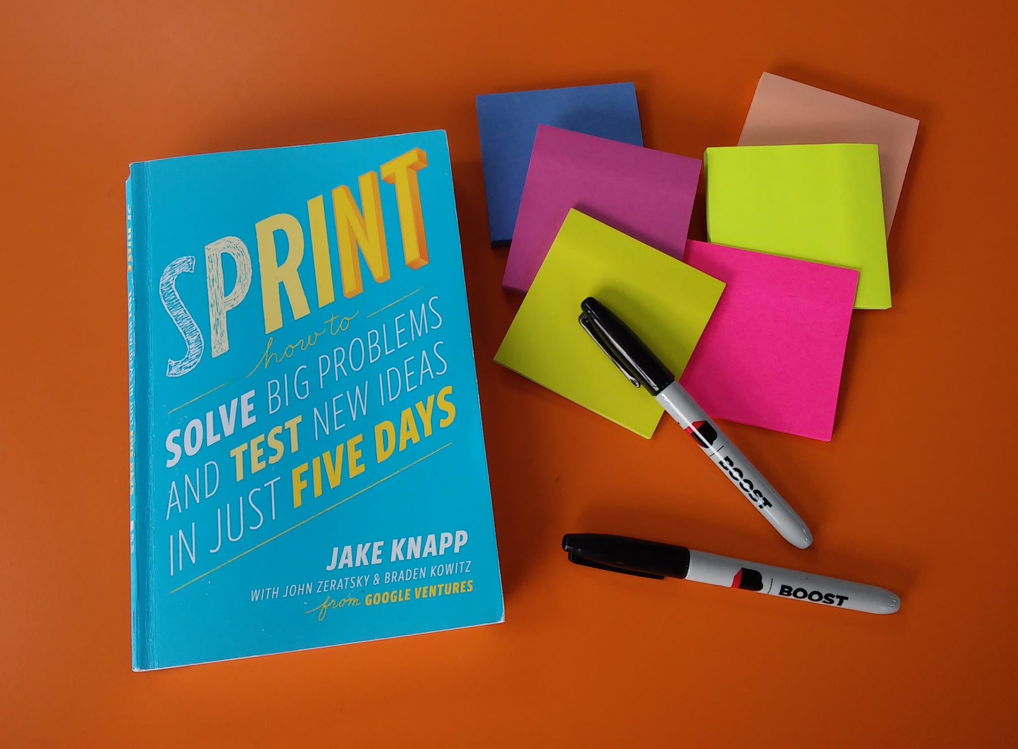 The Google Design Sprint book with post-its and pens.