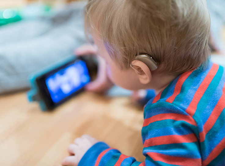 Baby with a hearing aid watching a video on a smartphone. Accessible digital services help GLAM institutions engage with all users.